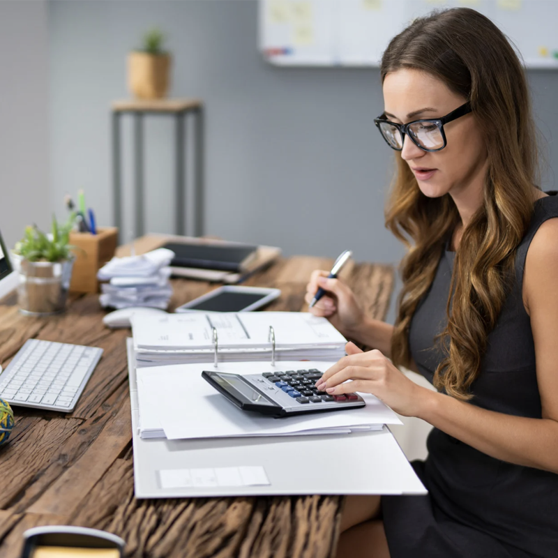 A woman at a desk using a calculator. A woman at a desk using a calculator.
